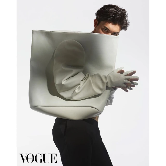 Fashion-forward studio portrait featuring an adult with a geometric, abstract bag and gloves against a bright white backdrop, showcasing style.