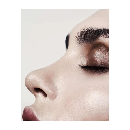 Close-up profile of a woman's face showing eye makeup and natural skin texture against a plain background