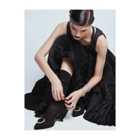 Woman in black dress and dark socks adjusting shoes against a neutral background by Rui Faria