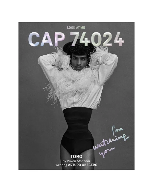 Dramatic black and white fashion portrait of a person with a black cap and feather boa posing against a grey studio backdrop. 