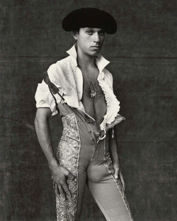 Portrait of a man wearing a black hat and traditional Spanish clothing, posing indoors against a dark backdrop with soft lighting.
