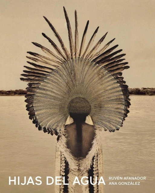 Woman wearing feathered headdress and fringe garment near river, soft light, earthen tones. Indigenous fashion editorial, environmental portrait.