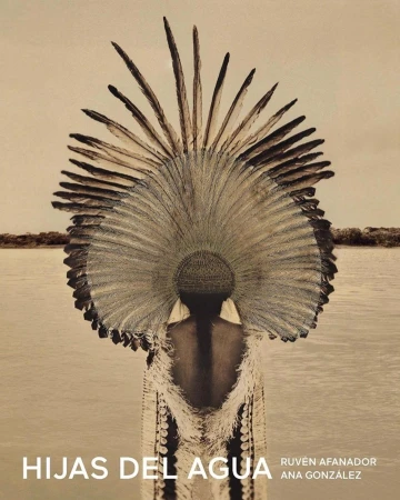 Woman wearing feathered headdress and fringe garment near river, soft light, earthen tones. Indigenous fashion editorial, environmental portrait.
