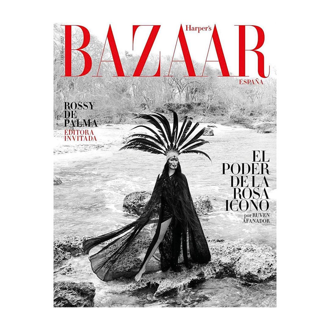 Harper's Bazaar cover featuring a woman with a feathered headdress in black and white, posing outdoors on a rocky riverbank.