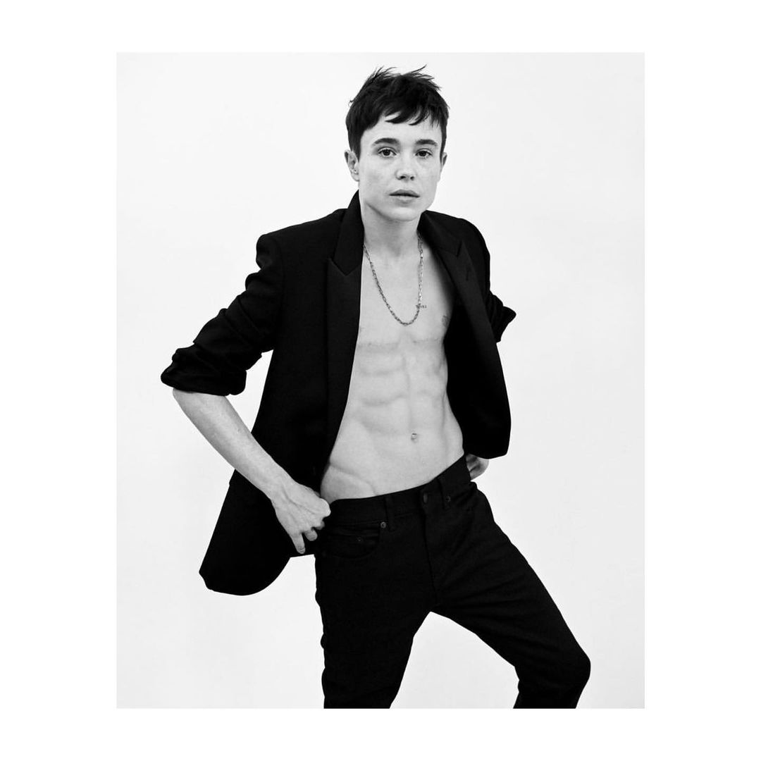 Portrait of adult male with bare chest and black jacket, posed against a stark white background in a studio setting, in black and white.