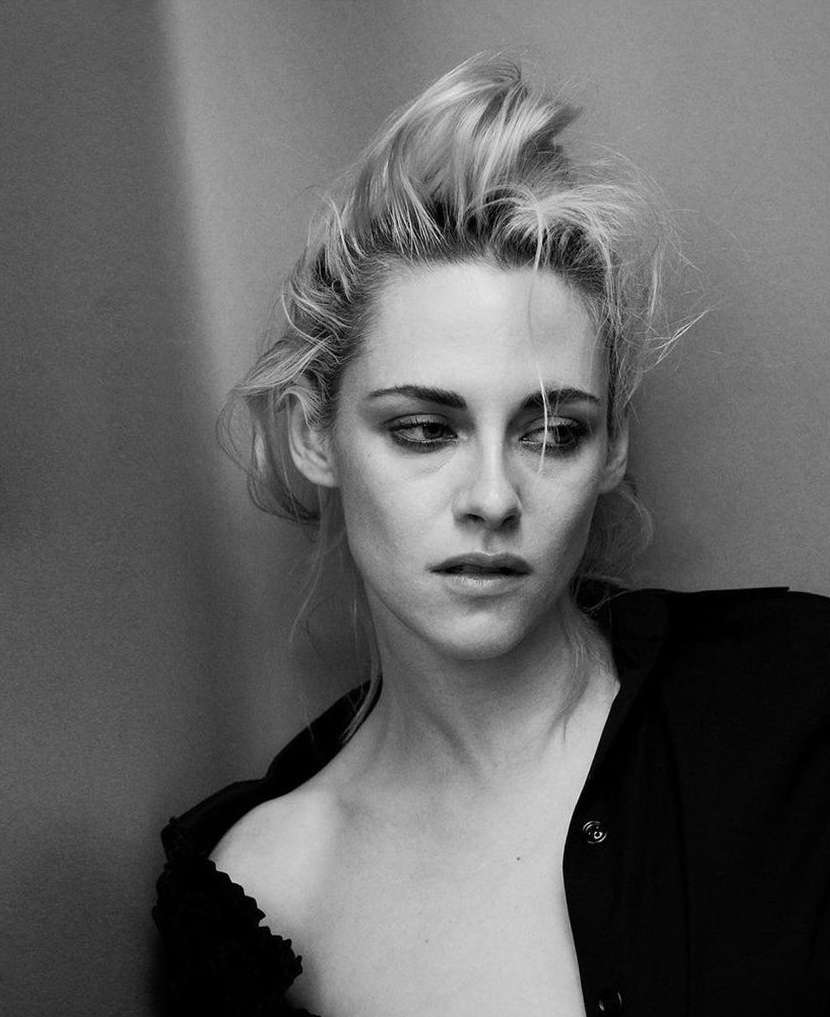 Black-and-white portrait of a blonde adult woman with fair skin wearing a black shirt, looking down and to the side against a grey background.
