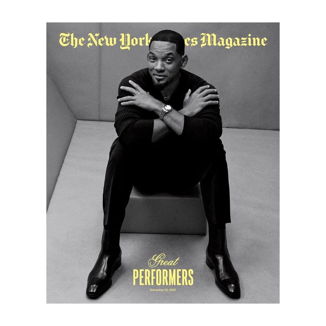 Magazine cover featuring Will Smith in a black sweater and trousers, seated with arms crossed and black boots, against a grey backdrop.