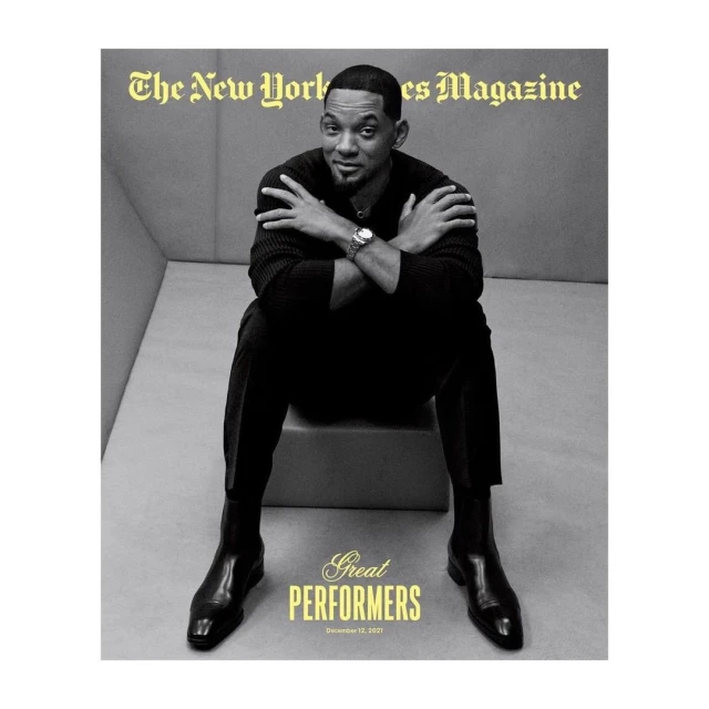 Magazine cover featuring Will Smith in a black sweater and trousers, seated with arms crossed and black boots, against a grey backdrop.