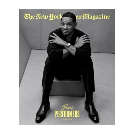 Magazine cover featuring Will Smith in a black sweater and trousers, seated with arms crossed and black boots, against a grey backdrop.