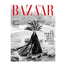 Monochrome magazine cover featuring a woman wearing an elaborate feathered headdress standing on river rocks by Ruven Afanador