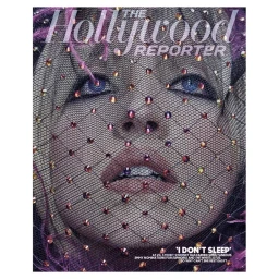 Close-up portrait of a woman's face covered by a black jeweled mesh veil with glittering rhinestones and purple feathers.