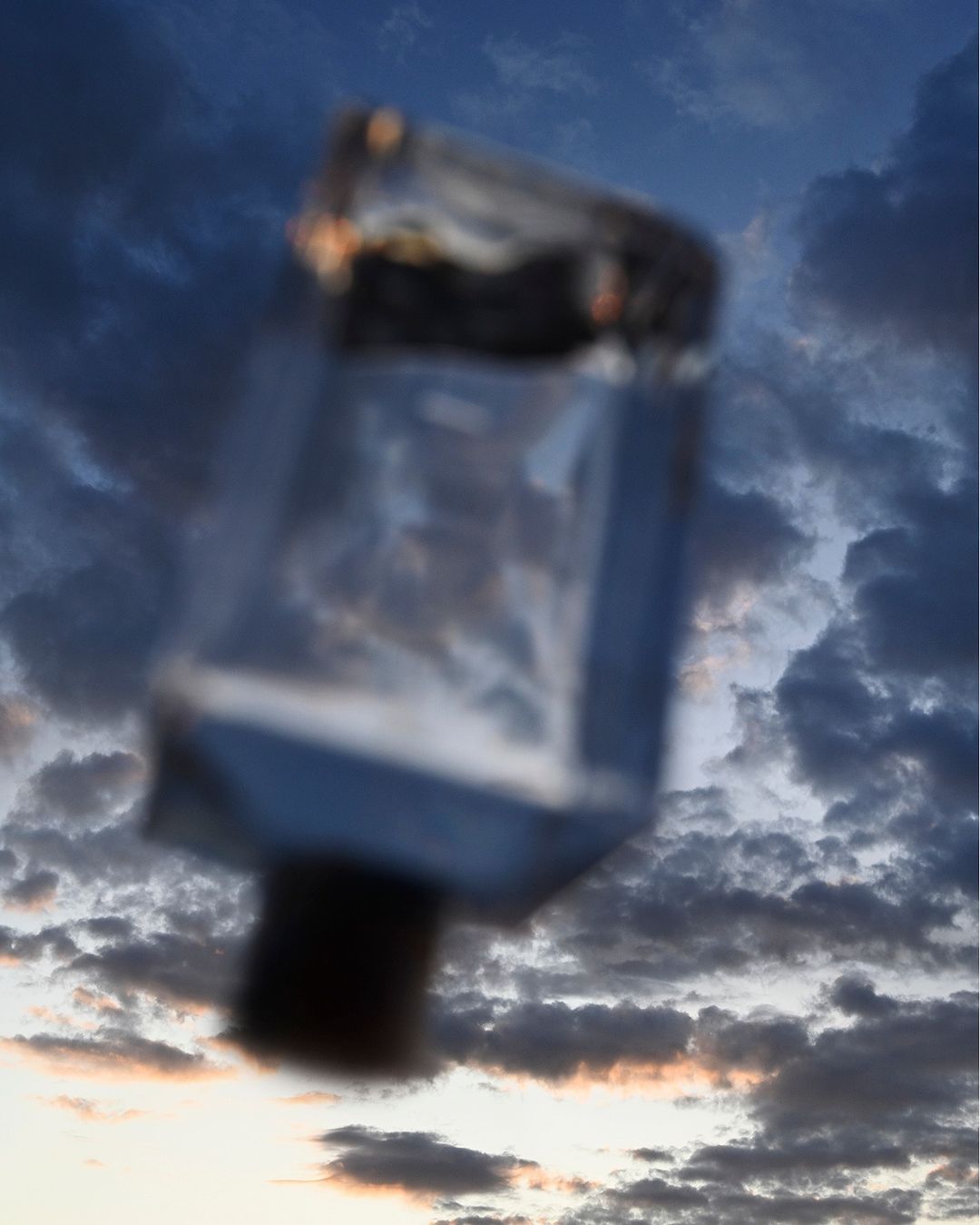 Blurred image of glass bottle floating against a cloudy sunset sky, blending industrial object with natural atmospheric background.