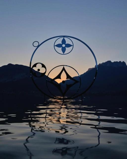 Abstract rendering of a logo reflected on water with a mountain range and twilight sky in the background, creating a serene atmosphere.
