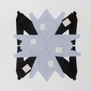 Flat lay of folded light blue shirts and black pants arranged in a geometric star pattern on a white background, creating a symmetrical design.