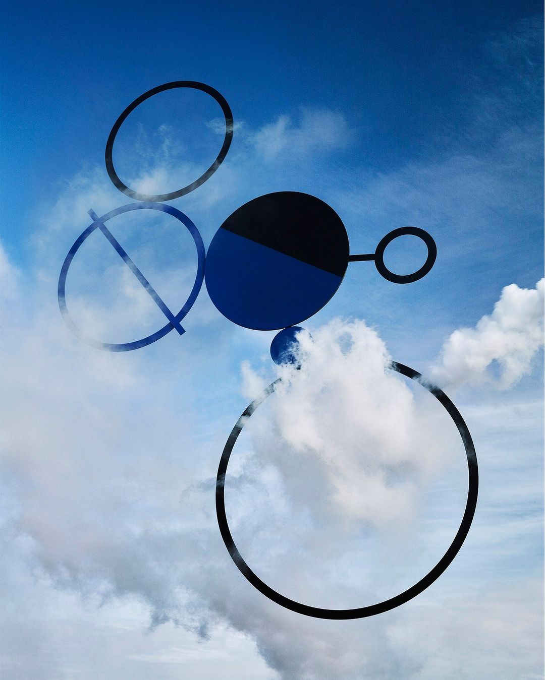 Abstract geometric shapes in black and blue float against a vibrant blue sky with scattered clouds, creating a surreal, modern design.