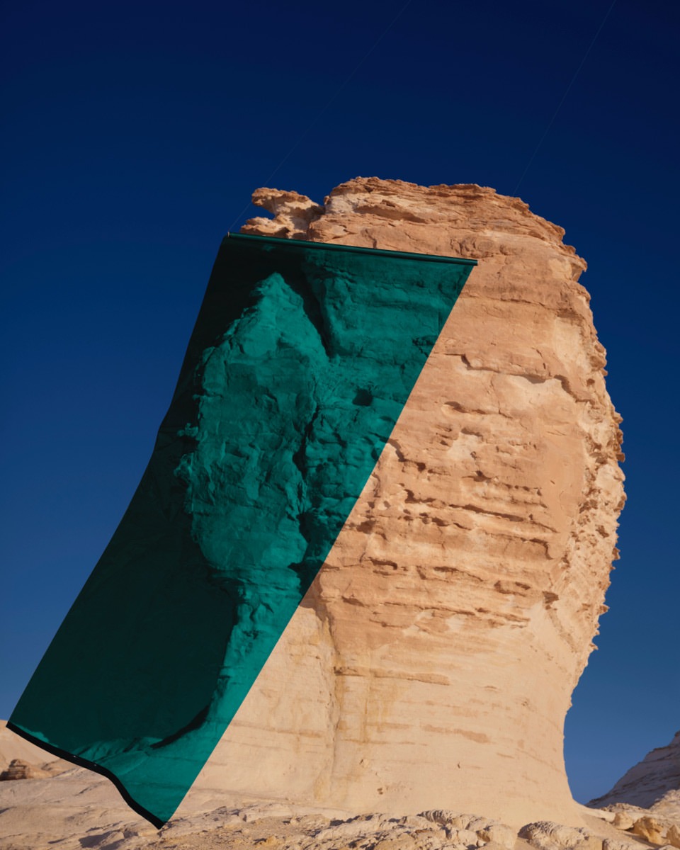 A uniquely shaped rock formation with a teal overlay stands against a clear blue sky in a desert-like environment, highlighting natural textures.