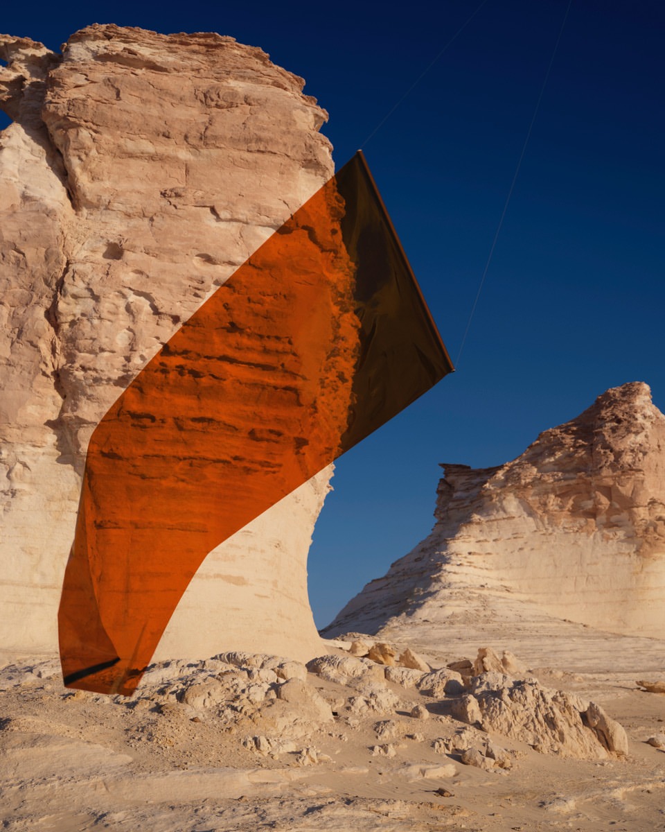 Monumental rock formations stand tall in a desert landscape under a clear blue sky, with an abstract rectangular art piece overlayed.
