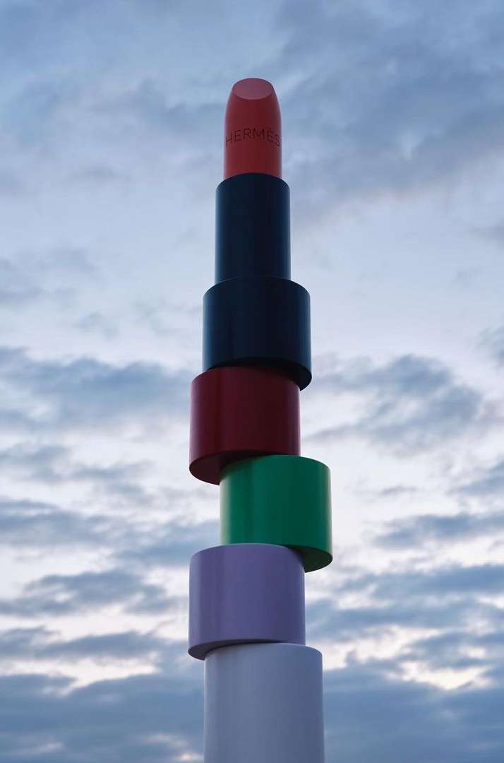 Tower of stacked lipsticks against a cloudy sky. Cosmetic product photography featuring beauty and luxury lifestyle with a whimsical composition.