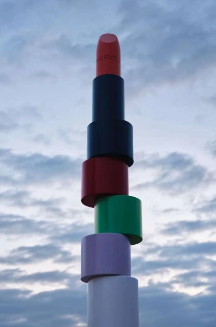 Tower of stacked lipsticks against a cloudy sky. Cosmetic product photography featuring beauty and luxury lifestyle with a whimsical composition.