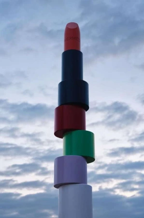 Tower of stacked lipsticks against a cloudy sky. Cosmetic product photography featuring beauty and luxury lifestyle with a whimsical composition.