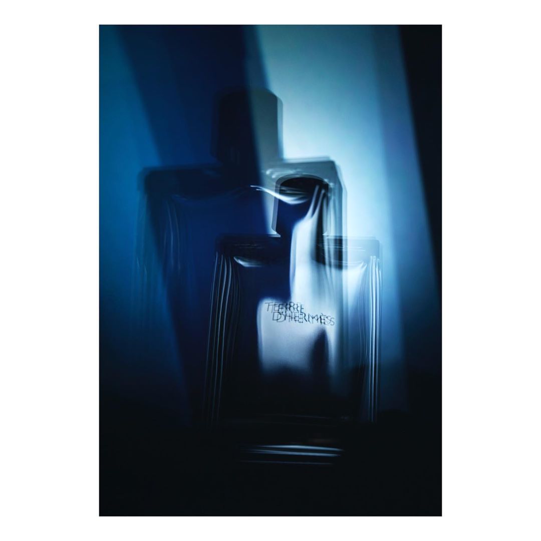 A blurred studio shot of a Terre d'Hermès perfume bottle set against a gradient blue background and stark shadows.