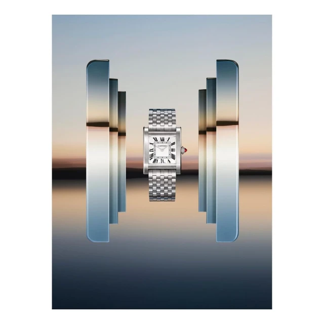 Silver Cartier Tank watch on a metal bracelet, presented with vertical bars of reflective chrome, set against a blurred sunset sky.