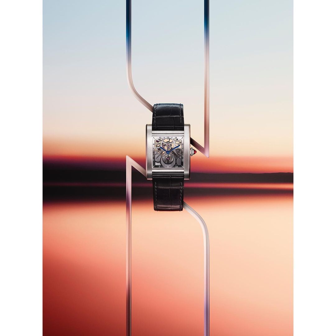 Wristwatch with a skeleton dial and black leather strap, photographed on a colorful background with transparent architectural elements.