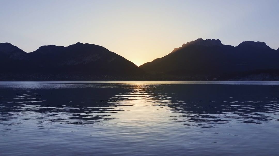 Scenic landscape with water reflecting silhouetted mountains under a soft, golden-lit sky at dusk or dawn.
