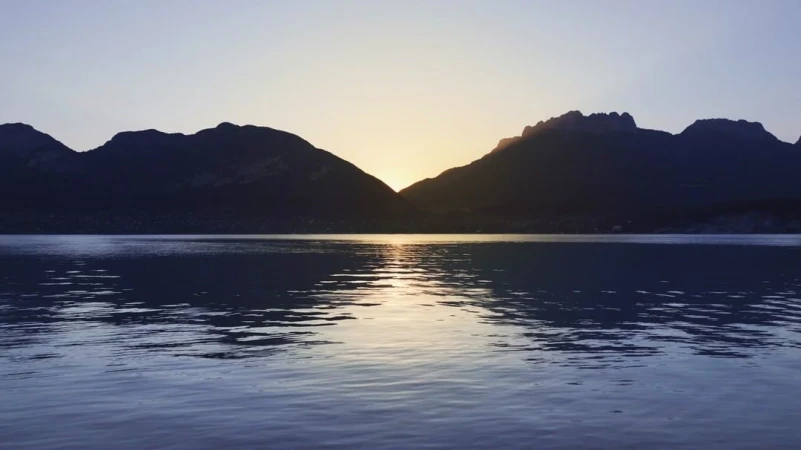 Scenic landscape with water reflecting silhouetted mountains under a soft, golden-lit sky at dusk or dawn.
