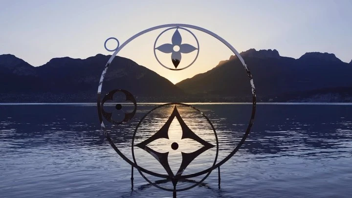 Metal sculpture featuring a floral pattern in a lake at sunset with mountains in the background, creating a serene and artistic landscape.