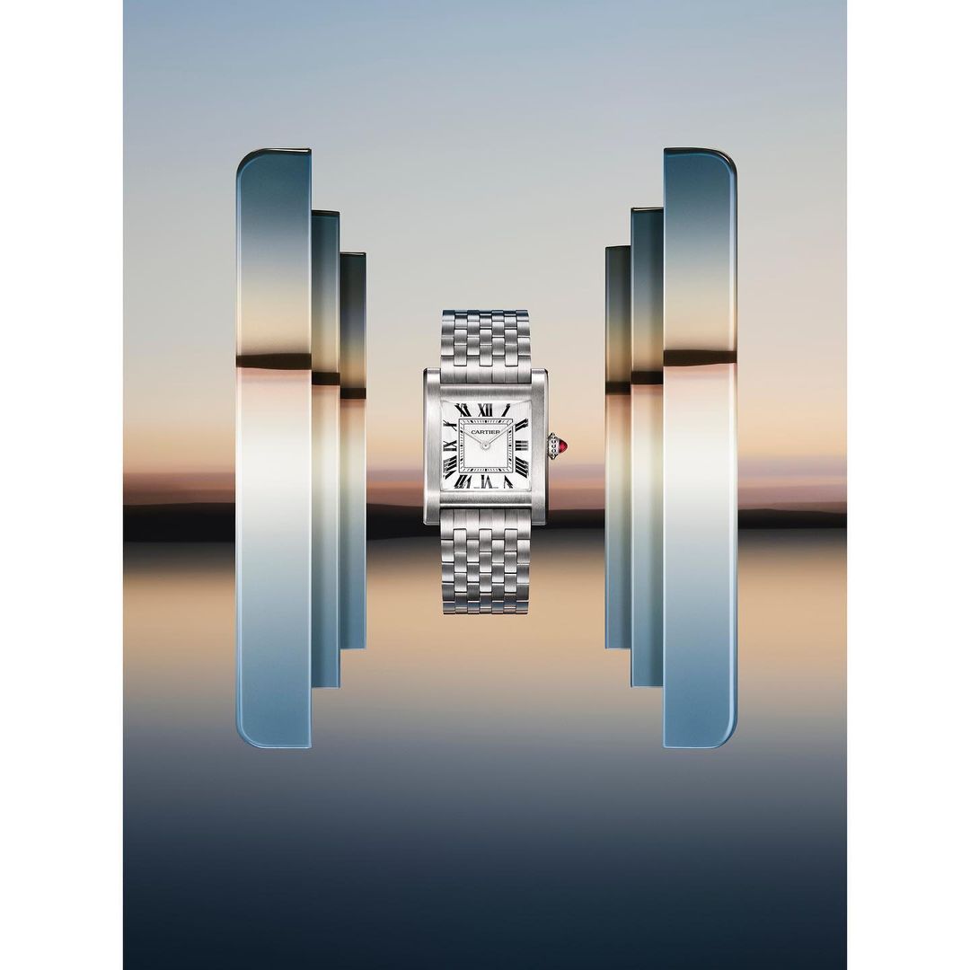 Elegant, silver Cartier Tank watch with a white face, floating between mirrored pillars on a reflective, blurred background, timekeeping precision.