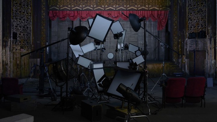 Indoor photography studio set up with lighting equipment, light reflectors, and red chairs in an old theatre with ornate columns and stage.
