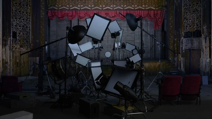 Indoor photography studio set up with lighting equipment, light reflectors, and red chairs in an old theatre with ornate columns and stage.