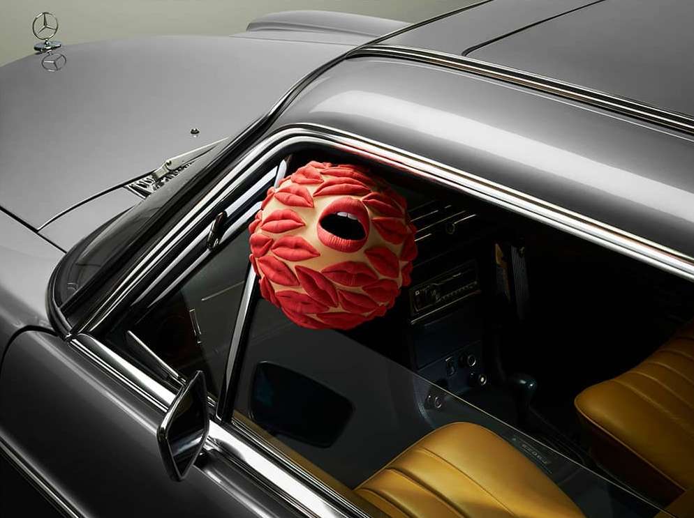 Gray vintage Mercedes-Benz with a red lips sphere inside the car's window. Automotive advertisement with conceptual elements.