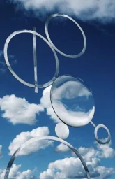 Polished metal sculptural circles and intersecting lines reflecting a blue sky with fluffy white clouds