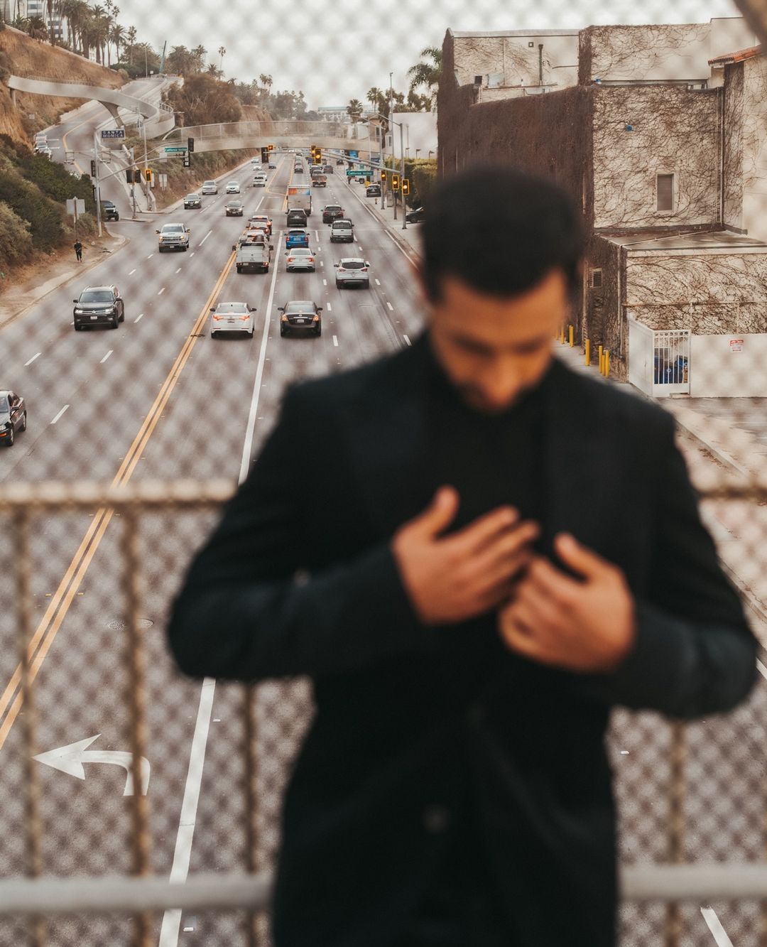 Out-of-focus man in black jacket standing on an overpass overlooking a busy multi-lane highway in New York