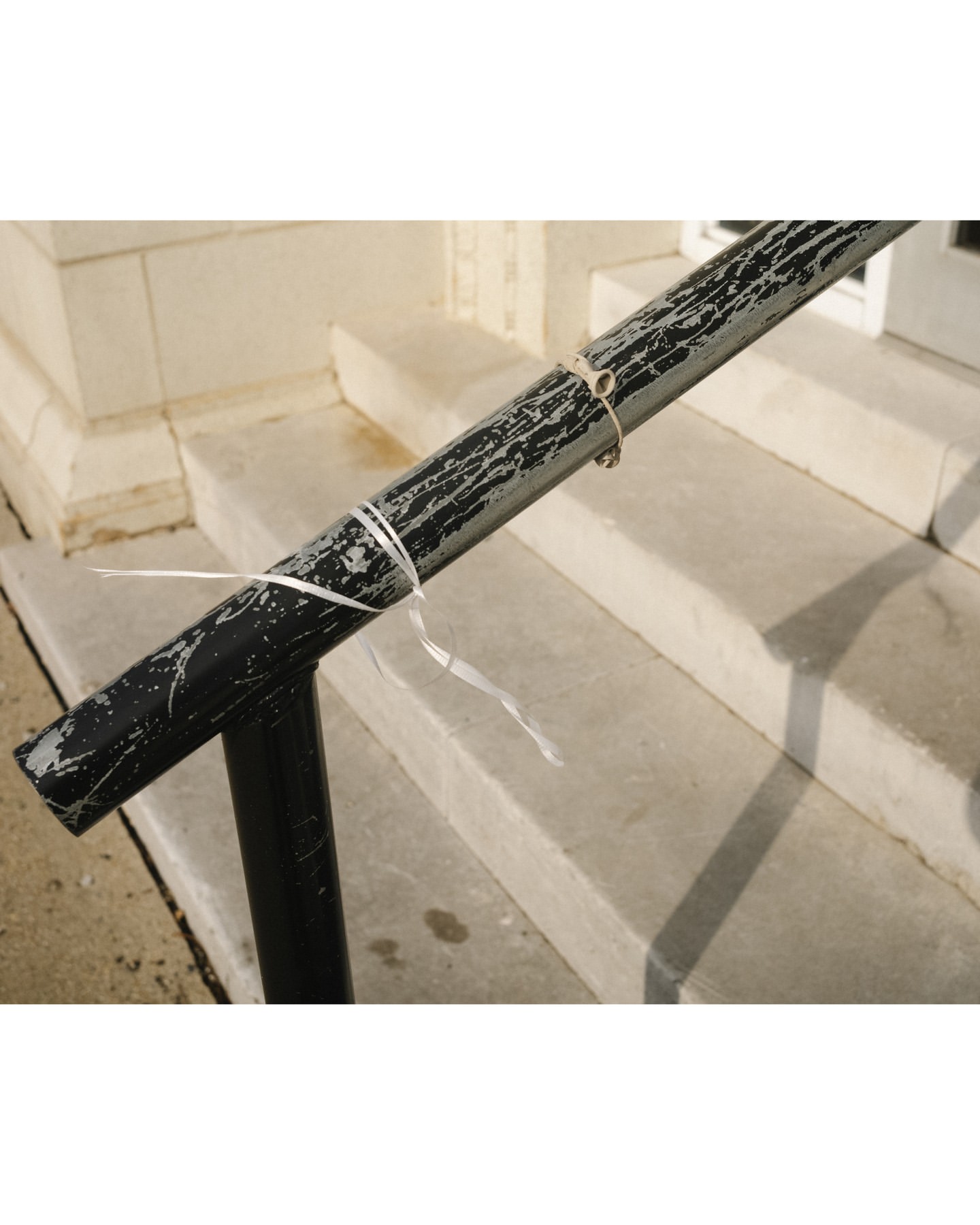 Close-up of a black metal handrail attached to concrete stairs, secured with white plastic ties, showcasing an outdoor, architectural detail.