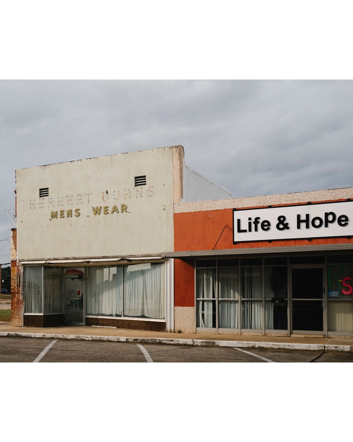 Exterior view of a two-story commercial building with vintage signage and modern additions against a cloudy sky in a town setting.