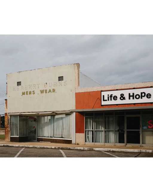 Exterior view of a two-story commercial building with vintage signage and modern additions against a cloudy sky in a town setting.