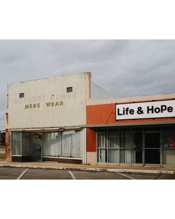 Exterior view of a two-story commercial building with vintage signage and modern additions against a cloudy sky in a town setting.