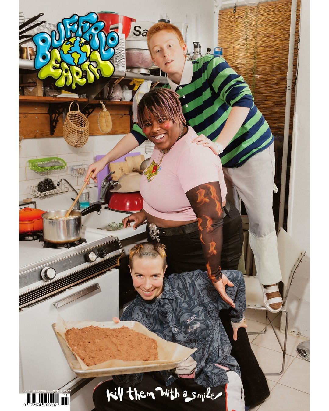 Three people pose in a kitchen. Two are behind the oven while one sits holding a tray of brownie batter. Magazine cover image.