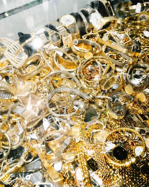 Close-up, high-angle shot of a collection of gold watches, jewelry and bracelets creating a textured and shimmering luxurious aesthetic.