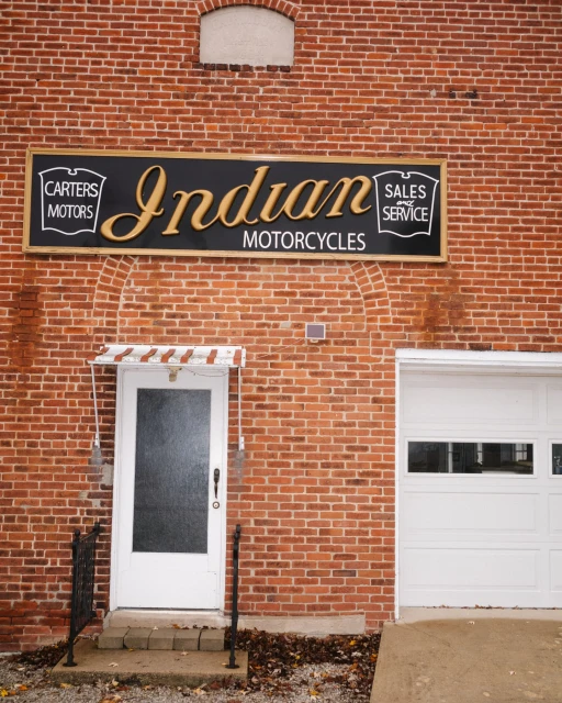 Exterior of a brick building featuring an Indian Motorcycles sign, a white door with a small awning, and a white garage door.