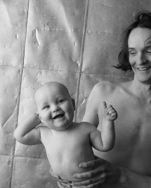 Black and white portrait of a happy baby being held by an adult with a metallic background, evoking a sense of joy and simplicity.