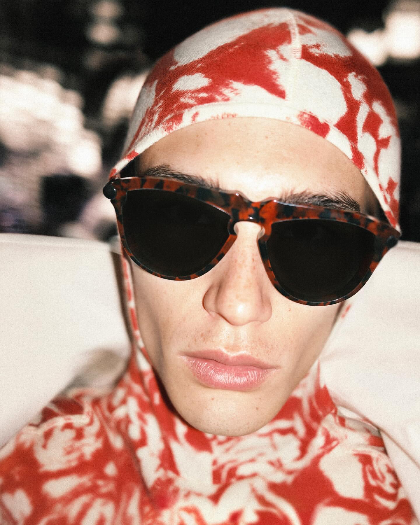 Close-up portrait of a man wearing tortoiseshell sunglasses and a red and white patterned cap by Ryan McGinley in New York.