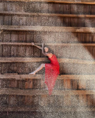 Woman in red dress strikes a dramatic pose on weathered wood stairs. Glittering particles create a visually arresting, textured effect.