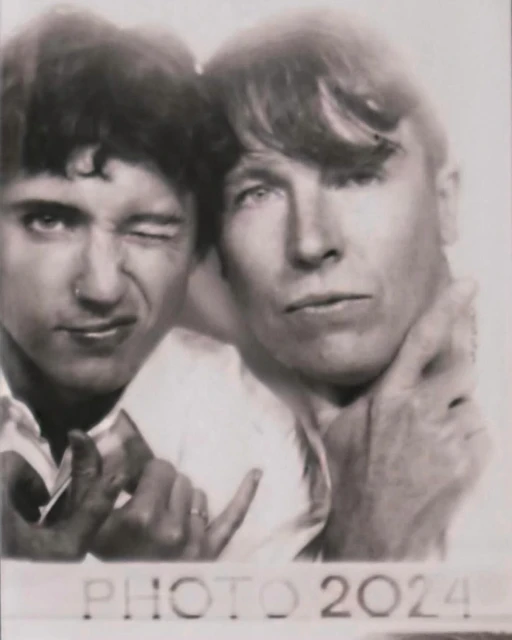 Monochrome close-up of two adult men, one winking, in a photo booth-style image with 'PHOTO 2024' text, evoking a vintage aesthetic.