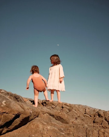 Two young children standing on rocky ground against a clear blue sky, photographed by Ryan Pavlovich.