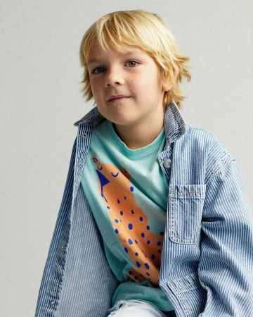 Young boy in a light blue printed t-shirt and vertically striped denim jacket, posing in front of a neutral background.