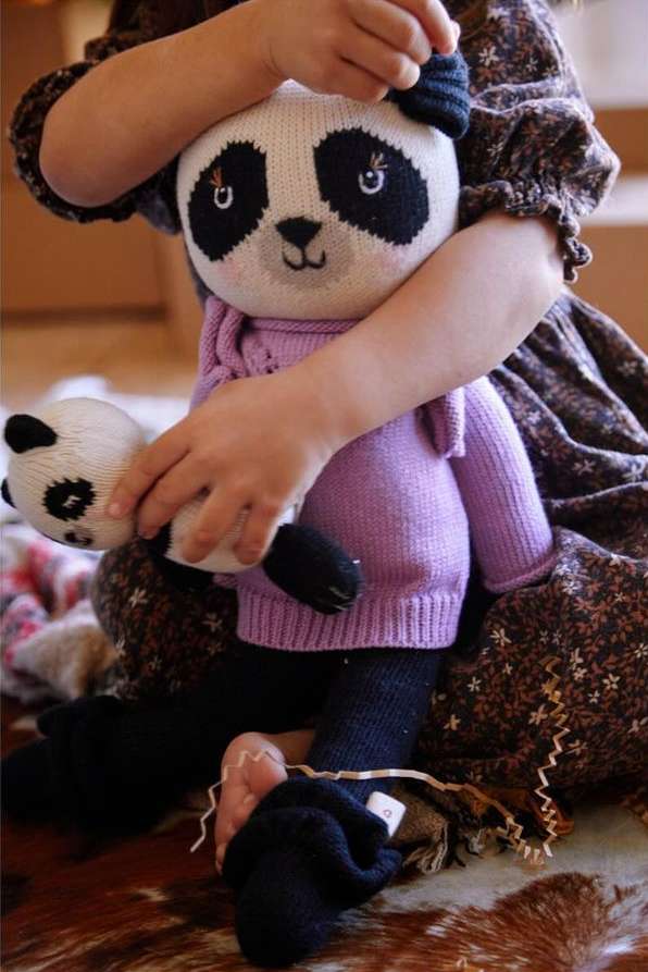 Young child holding two panda bear stuffed animals, wearing a purple sweater and brown dress with a cowhide rug in the background.